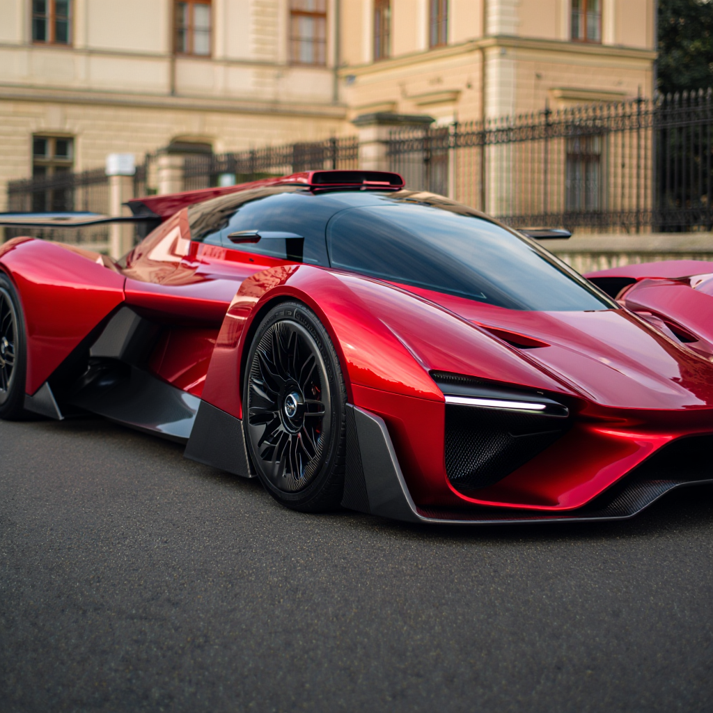 A futuristic concept hypercar rendered in metallic red stands prominently against a classical European architectural backdrop