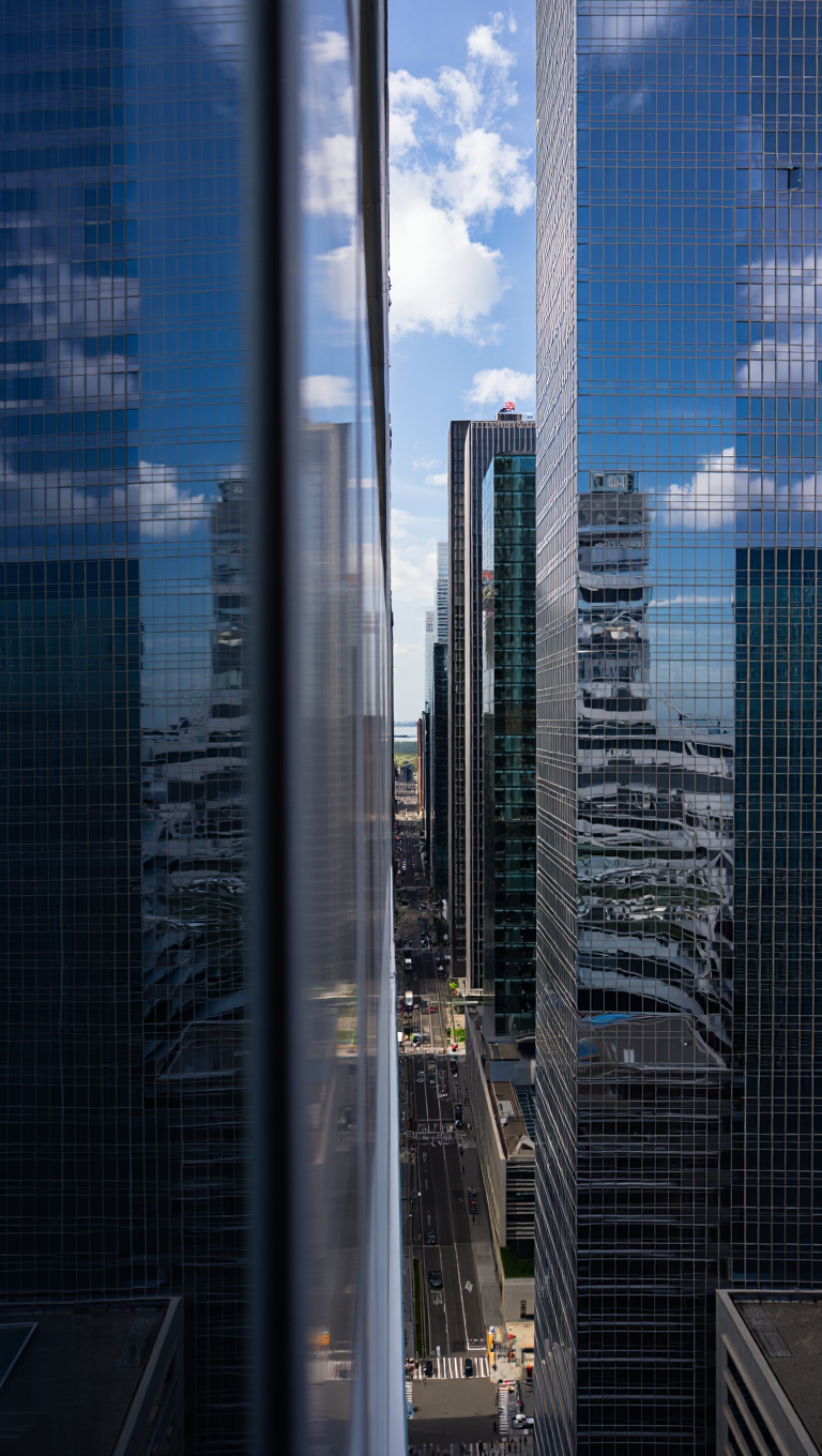 A high-angle, wide-shot architectural photography of a city street nestled between two towering skyscrapers with reflective glass facades